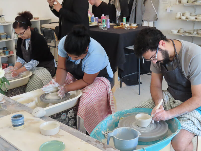 A group of people at a wheel throwing pottery class